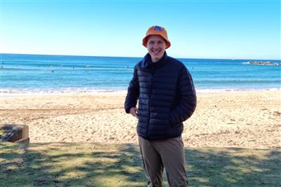 Man standing in front of the beach with surfers in the waves on a beautiful day